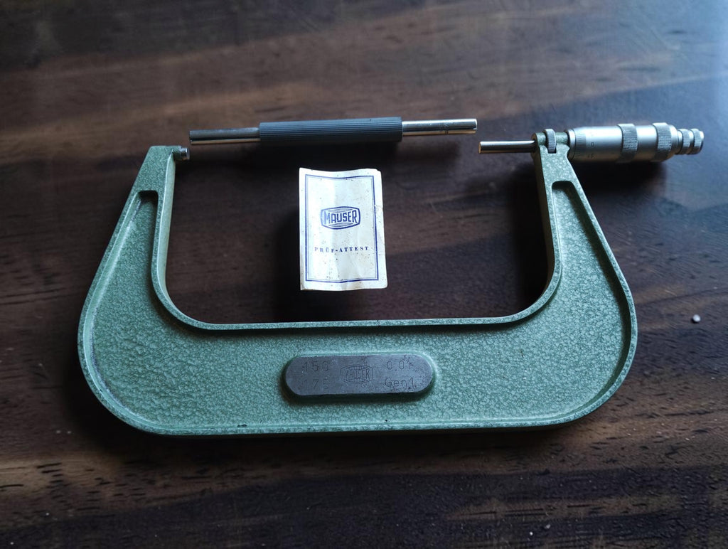 Mauser 150–175 mm outside micrometer with setting standard and Prüfattest booklet on a wooden table.

