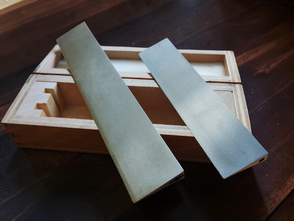 Two vintage MICROM precision knife-edge straightedges resting diagonally across an open wooden storage case.
