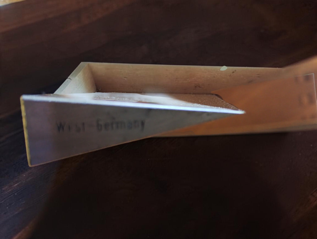 Side view of the fine inspection edge and tapered end of a vintage MICROM straightedge beside its wooden case.
