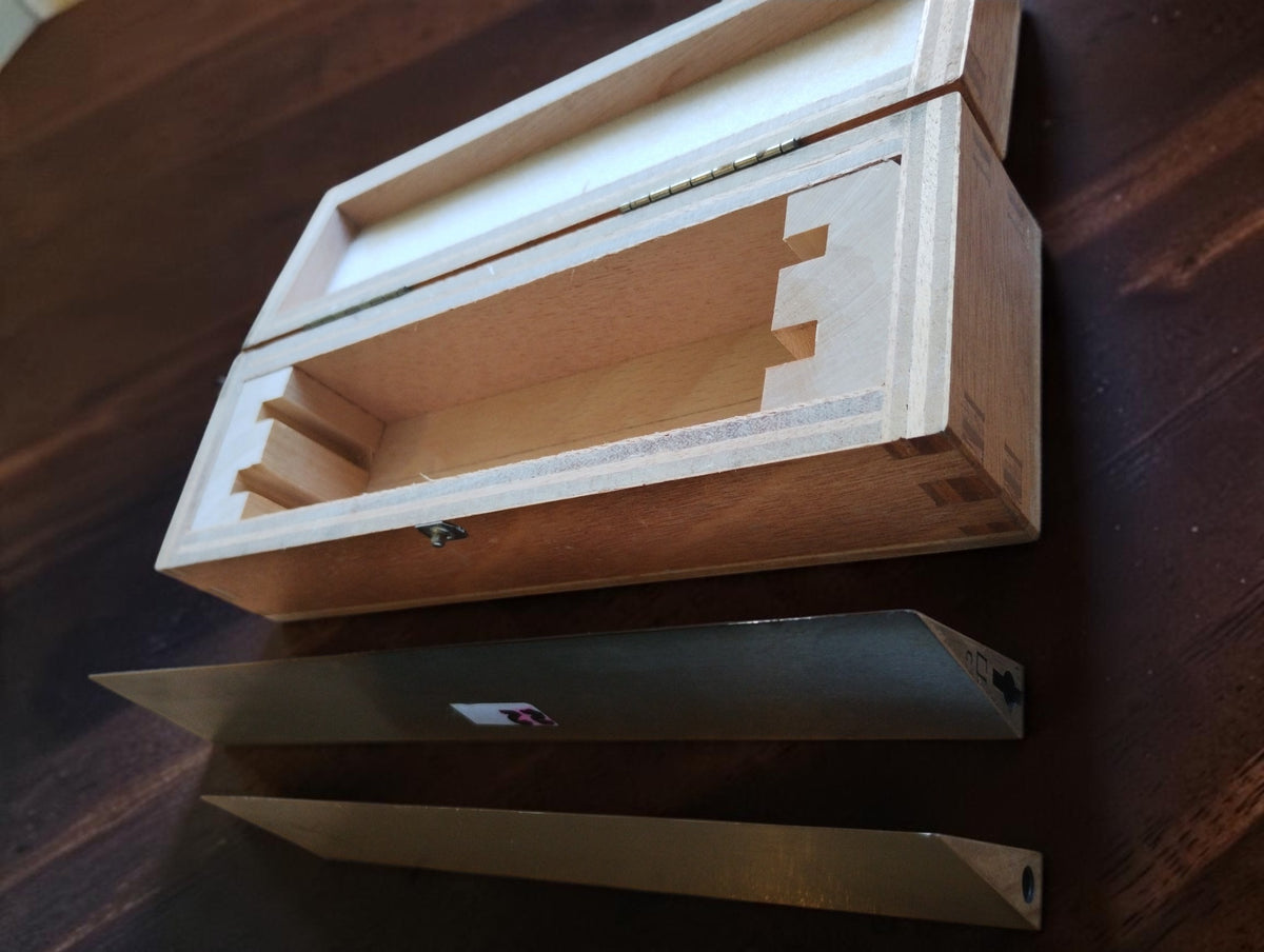 Two MICROM knife-edge straightedges laid beside their open wooden storage case, viewed at an angle.
