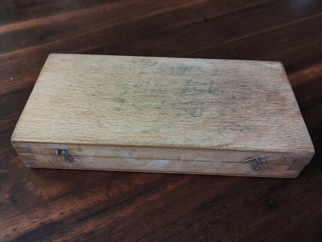 Closed wooden storage case with two metal latches and visible signs of wear and age.
