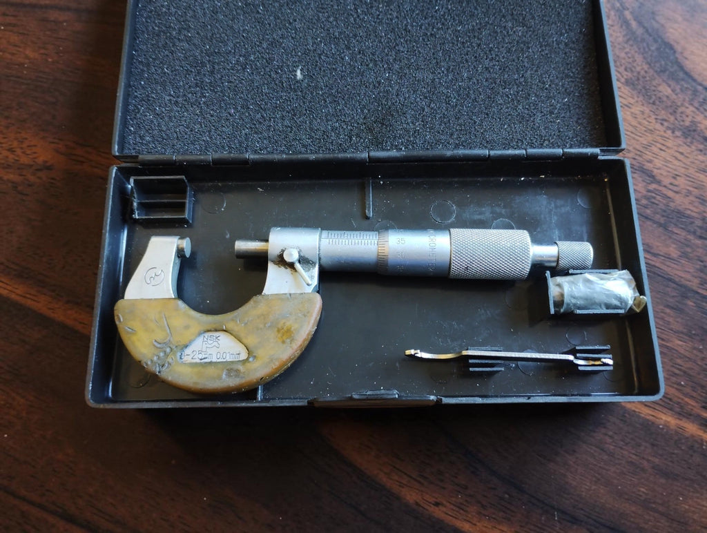 Vintage NSK outside micrometer in an open black case, with discolored frame cover, adjustment wrench and bagged accessory.
