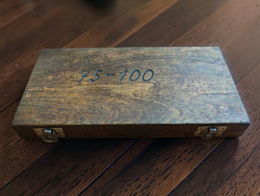 Closed wooden micrometer case with two metal catches and handwritten 75–100 marking on the lid
