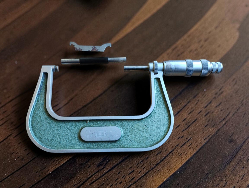 Vintage MAUSER outside micrometer with green frame, reference rod and adjustment wrench on a wooden table
