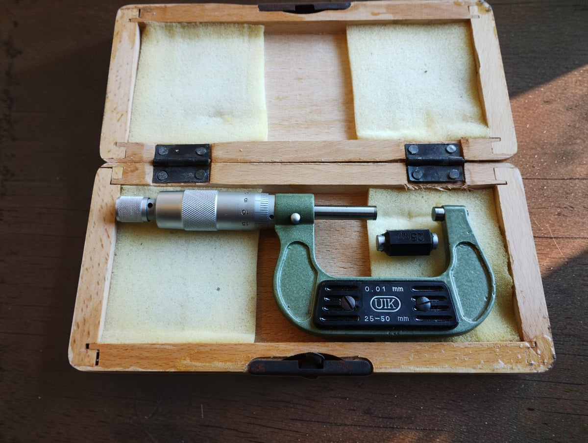 Vintage UIK 25–50 mm outside micrometer in an open wooden case with reference standard.
