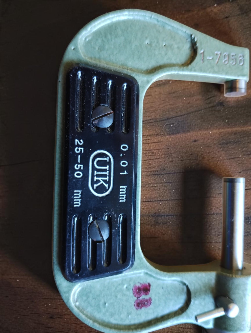 Detail of the green UIK micrometer frame with black nameplate, stamped number and reddish-purple marking.
