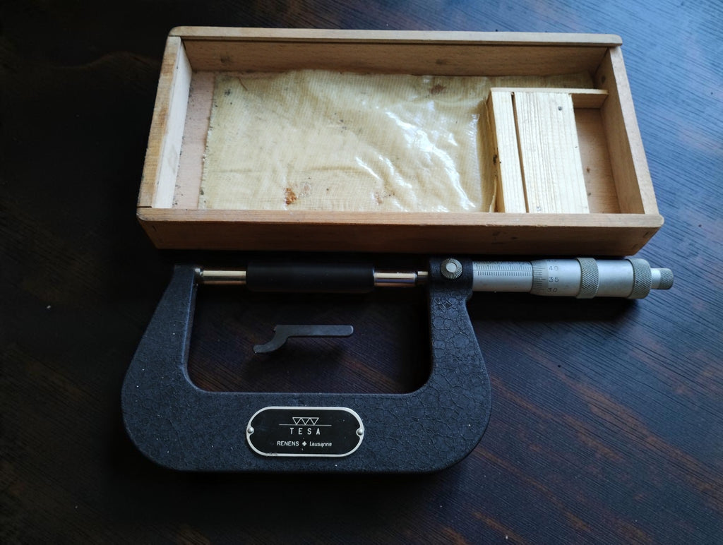 Vintage TESA outside micrometer beside its open wooden case, with setting standard and adjustment wrench.
