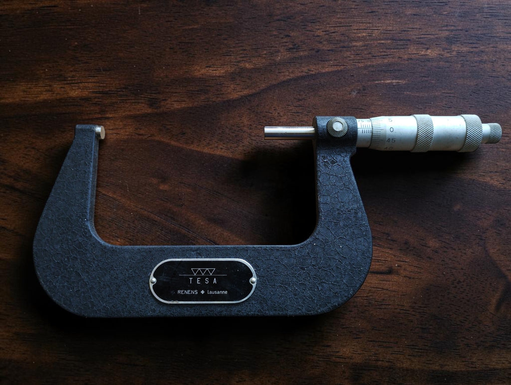 Front view of the TESA 75–100 mm outside micrometer with dark gray crackle finish and metal measuring thimble.
