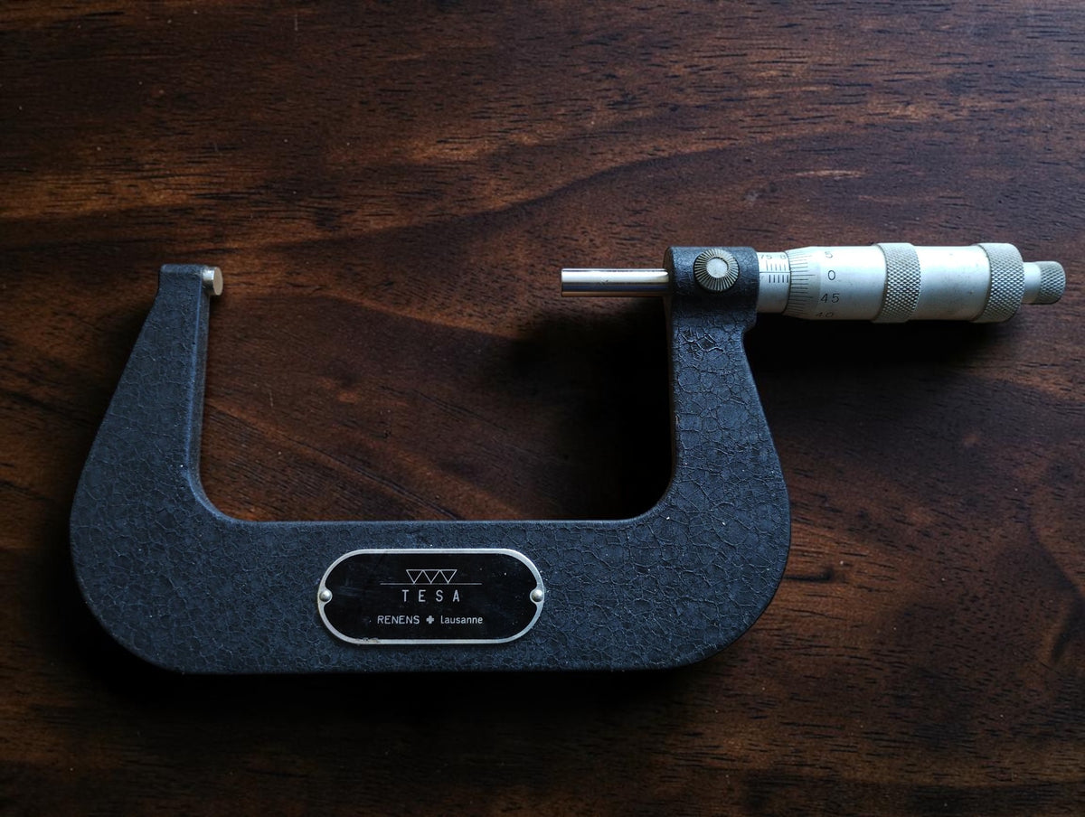 Front view of the TESA 75–100 mm outside micrometer with dark gray crackle finish and metal measuring thimble.
