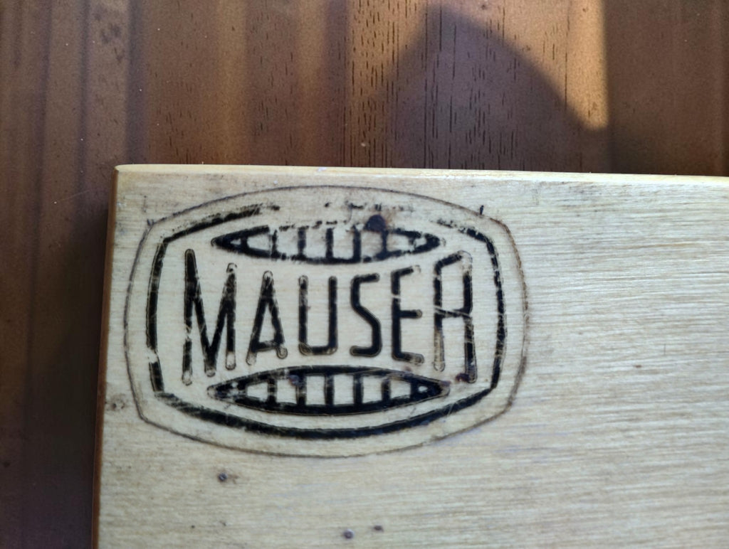 Close-up of the black Mauser barrel-shaped logo on the wooden micrometer case lid.
