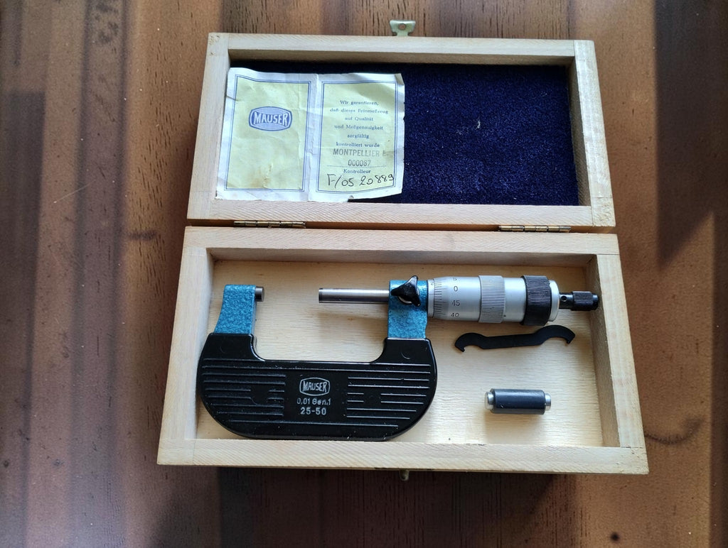 Vintage Mauser 25–50 mm outside micrometer in an open wooden case with setting standard, adjustment wrench and Mauser paperwork.
