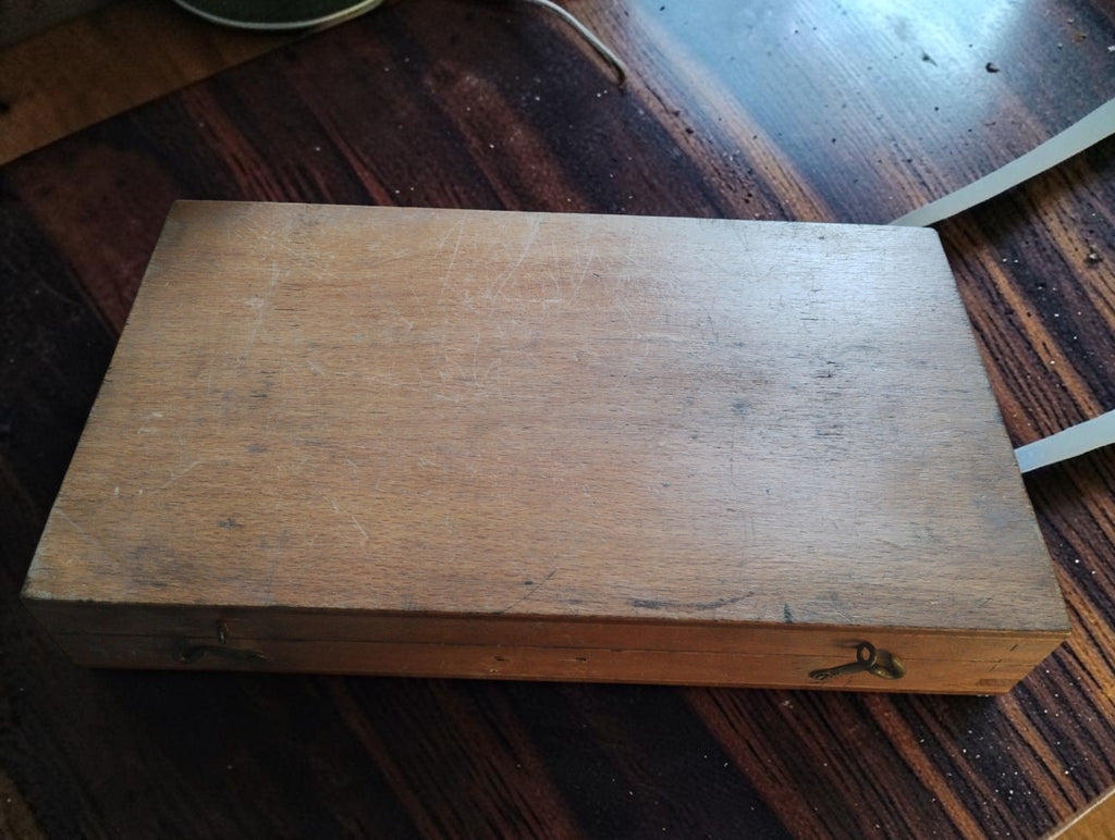 Closed wooden storage case for the NSK 100–125 mm outside micrometer, showing surface wear and metal clasps.

