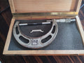 Vintage NSK 100–125 mm outside micrometer in an open wooden case with a 125 mm reference rod and adjustment wrench.

