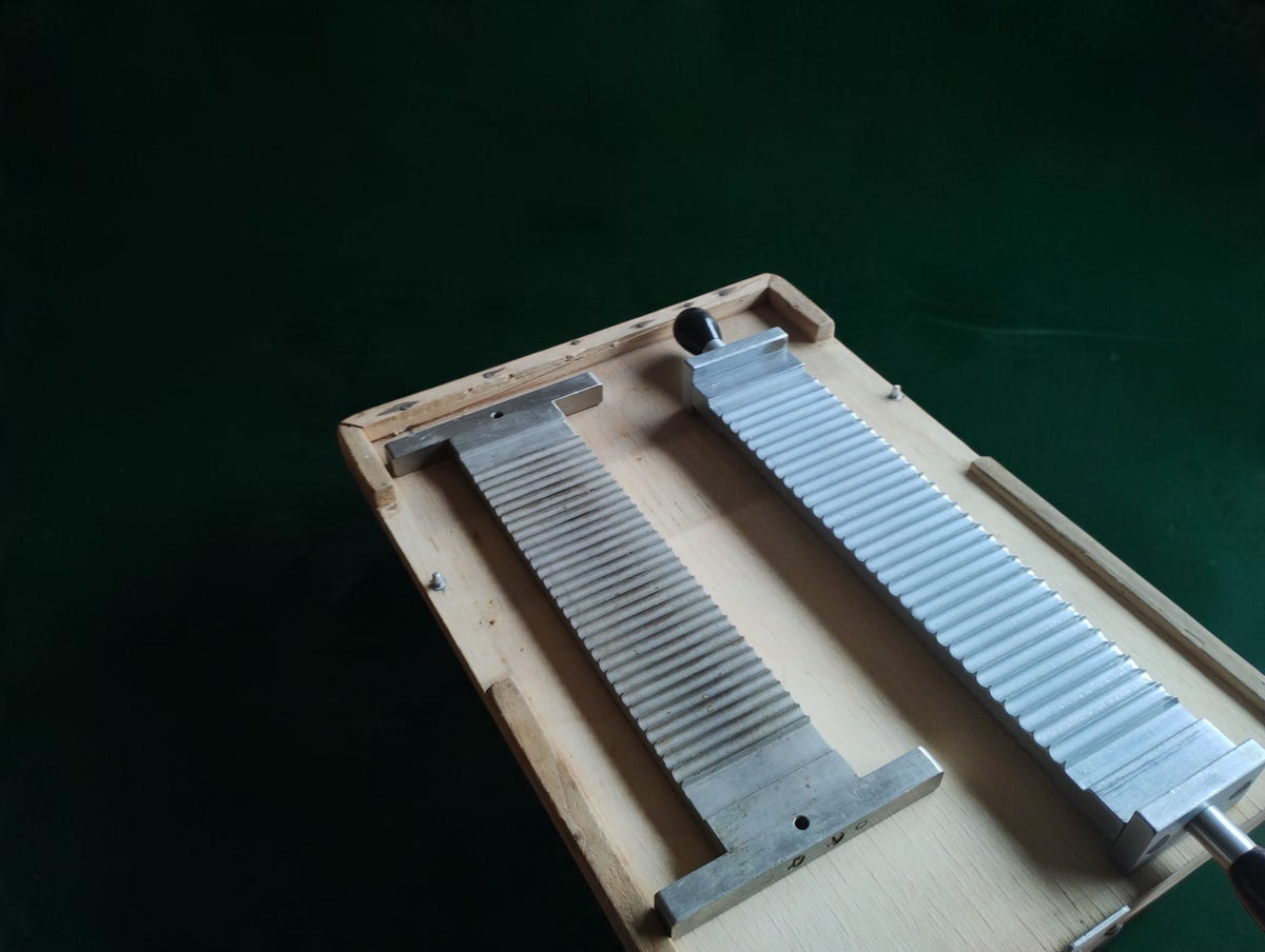 Grooved metal pill-making plate and handled component arranged inside a worn wooden apothecary base.

