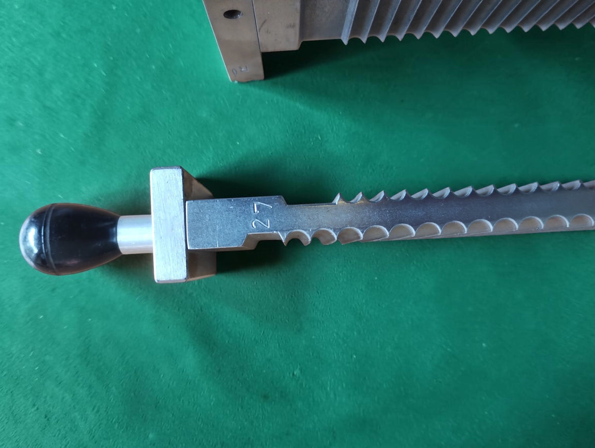 Close-up of a dark handle and grooved metal pill-making component with the engraved number 27.

