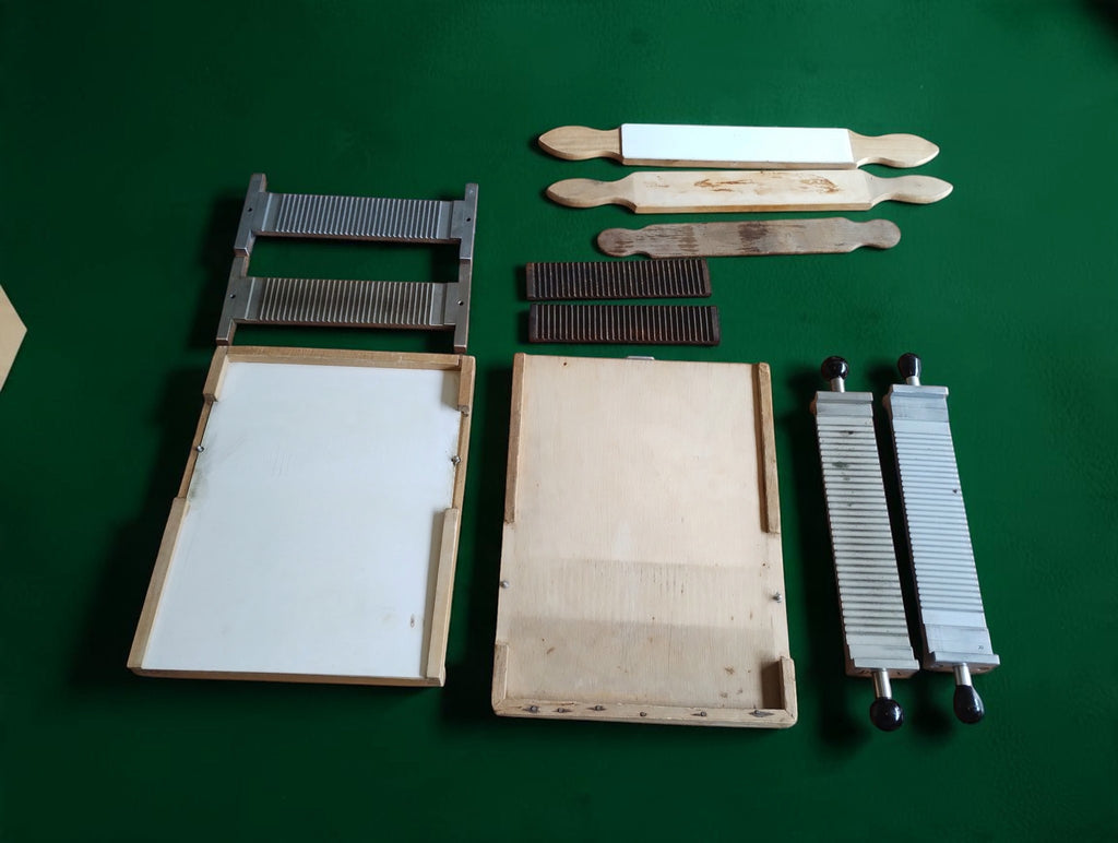 Vintage apothecary pill-making set with two wooden bases, grooved metal components and three wooden tools, displayed on a green background.
