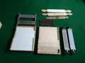 Vintage apothecary pill-making set with two wooden bases, grooved metal components and three wooden tools, displayed on a green background.
