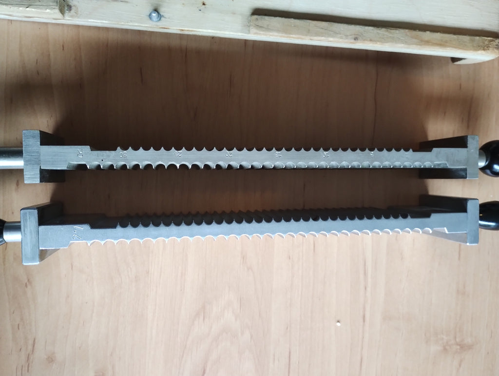 Side view of two grooved metal pill-making components with dark handles and engraved markings, resting on a wooden base.
