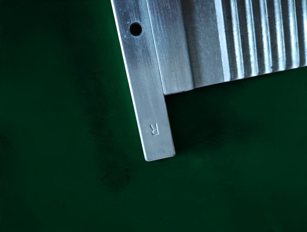 Close-up of a grooved metal plate with a mounting hole and an engraved letter R on its end support.
