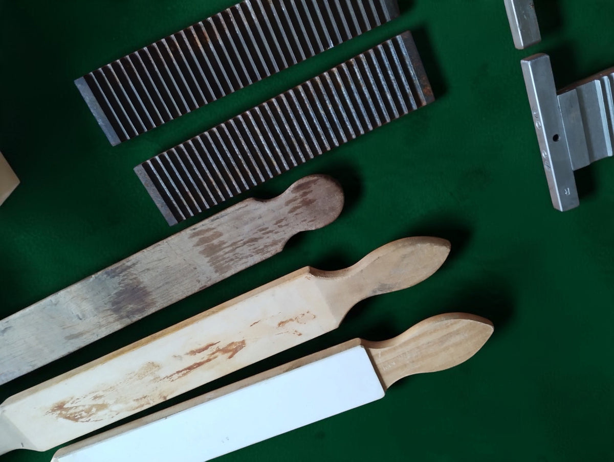 Three wooden apothecary tools, one with a white inset, beside two dark grooved metal plates, showing visible wear.
