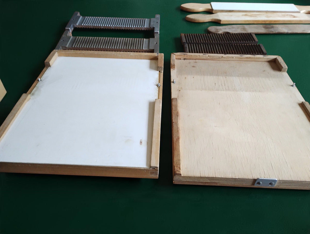 Two wooden apothecary bases side by side, one with a white inset, with metal plates and wooden tools behind them.
