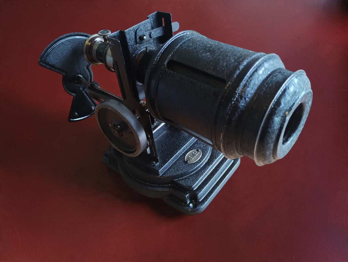 Antique VEDES hand-cranked projector with black metal housing, lens and mechanical components, shown from the side.
