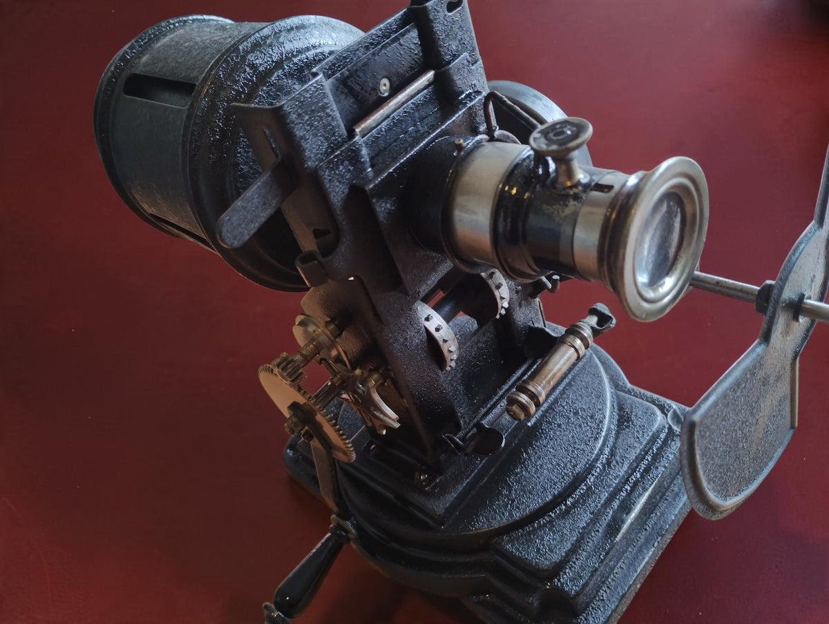 Side view of the antique VEDES projector with lens, slide holder, shutter blades and exposed mechanical parts.
