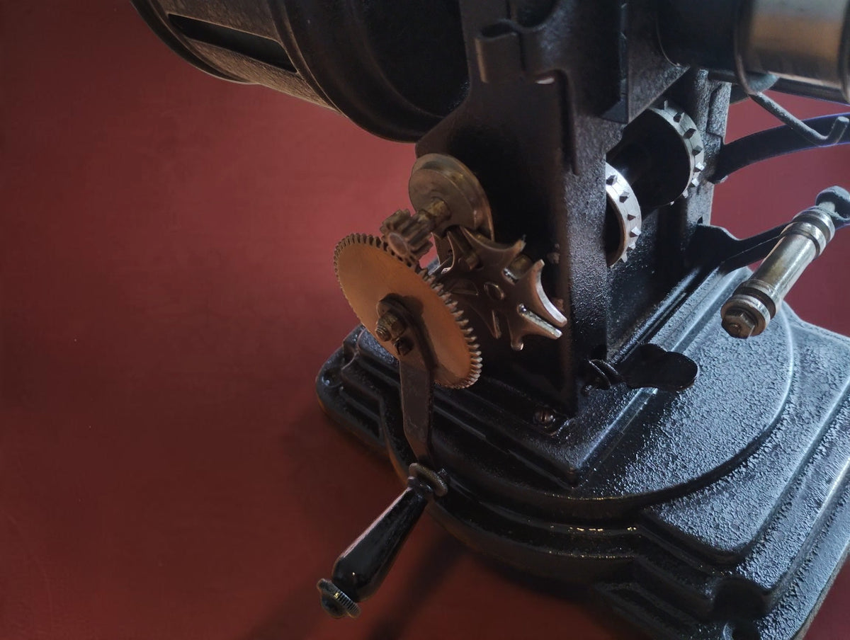 Close-up of the antique VEDES projector's exposed gears and hand crank, with wear to the black finish.
