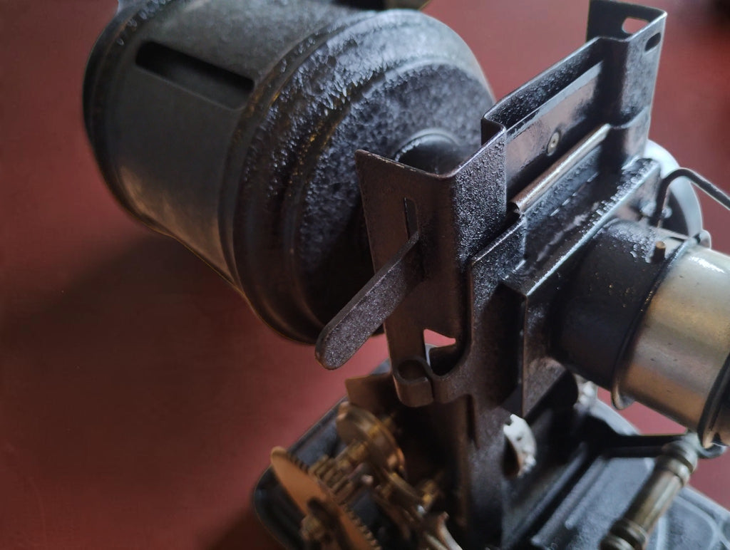 Close-up of the VEDES projector's slide holder beside the cylindrical housing and exposed mechanism.
