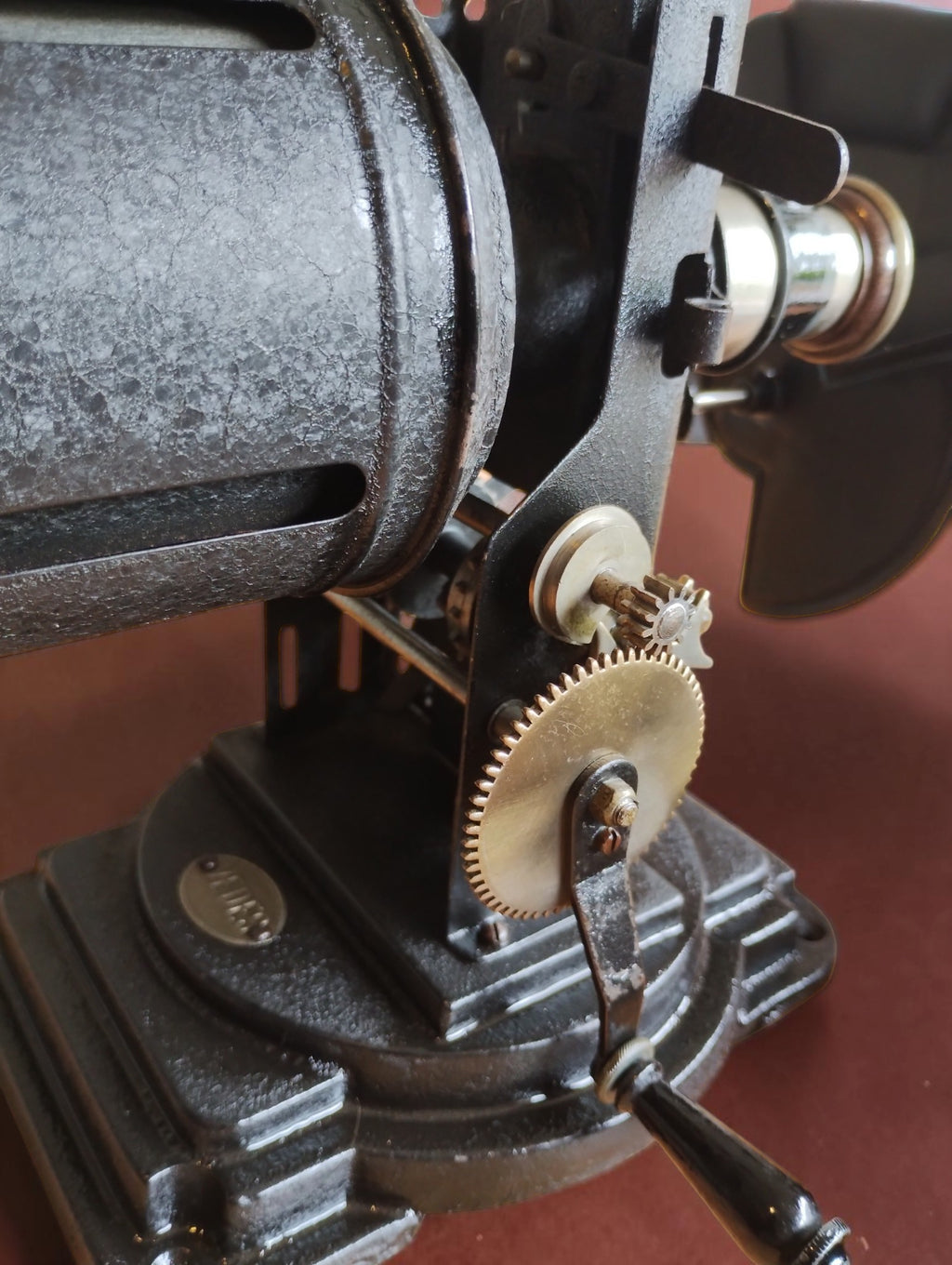 Detail of the VEDES projector's hand-cranked gear mechanism, black base and cylindrical housing.
