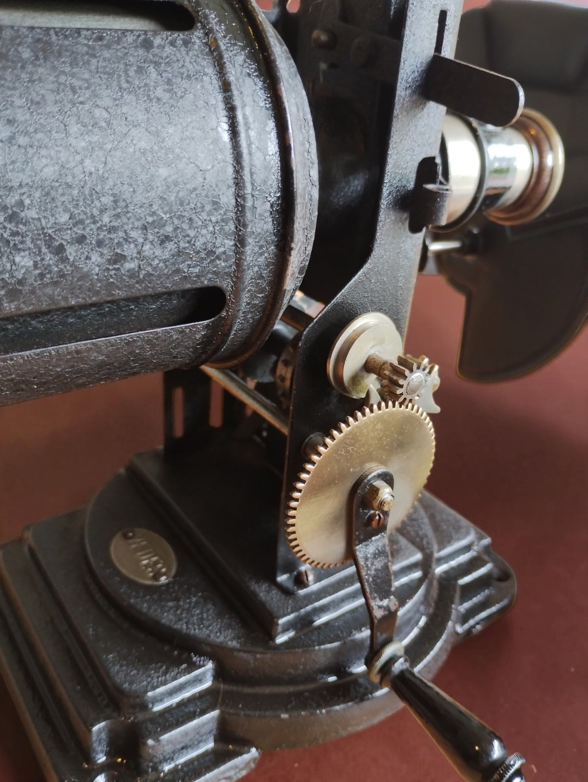 Detail of the VEDES projector's hand-cranked gear mechanism, black base and cylindrical housing.
