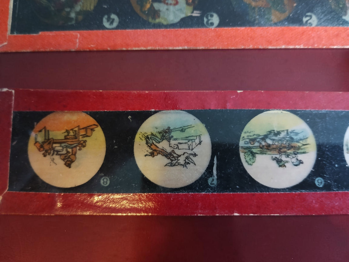 Close-up of a red-framed magic lantern glass slide with circular illustrated scenes and printed numbers.
