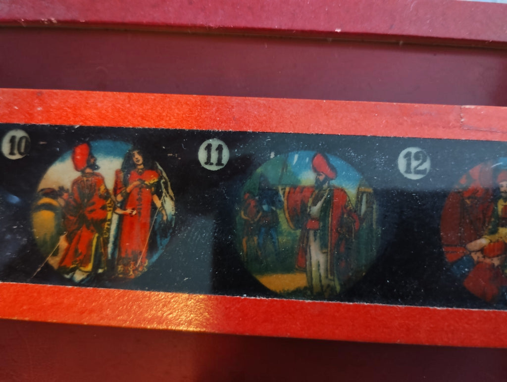 Detail of a red-framed magic lantern glass slide showing colorful figures in numbered scenes 10, 11 and 12.
