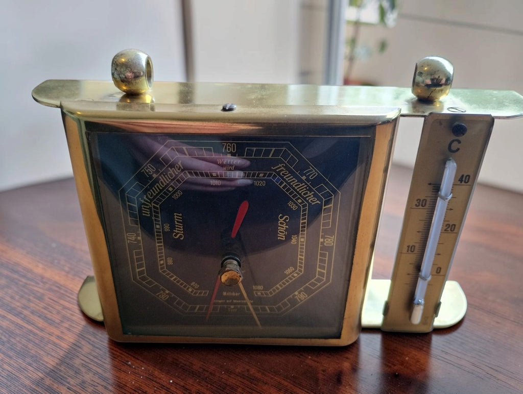 Angled front view of the Fischer barometer and thermometer, showing the gold-tone frame and rounded top supports.
