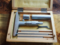 Analog depth micrometer set in an open wooden case with extension sleeves, three interchangeable measuring rods and adjustment wrench.
