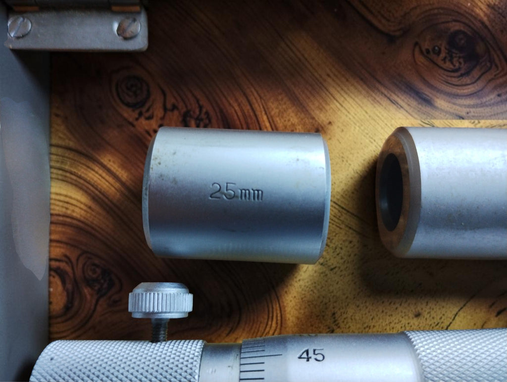 Close-up of the depth micrometer base marked 0-100 mm and 0.01 mm, beside the 25 mm extension sleeve.
