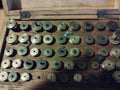 Close-up of antique watchmaker’s lantern runners in a wooden tray, showing stamped markings and square-ended shafts.
