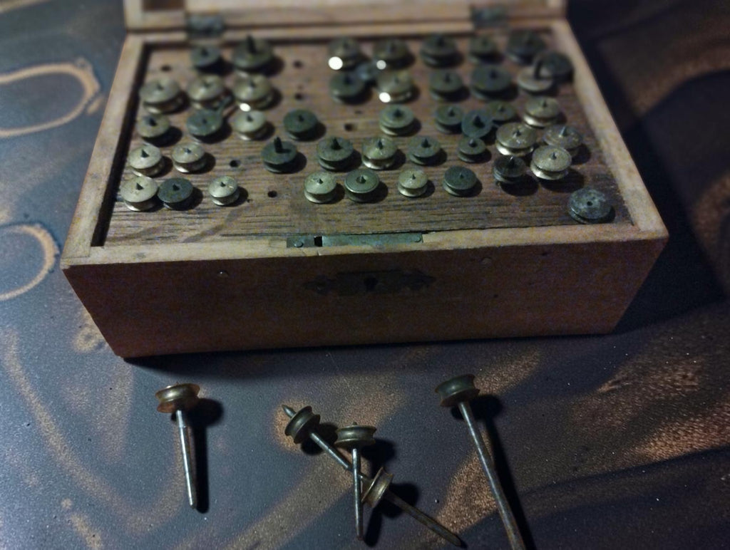 Open wooden case of antique watchmaker’s lantern runners with several loose shafted components displayed in front.
