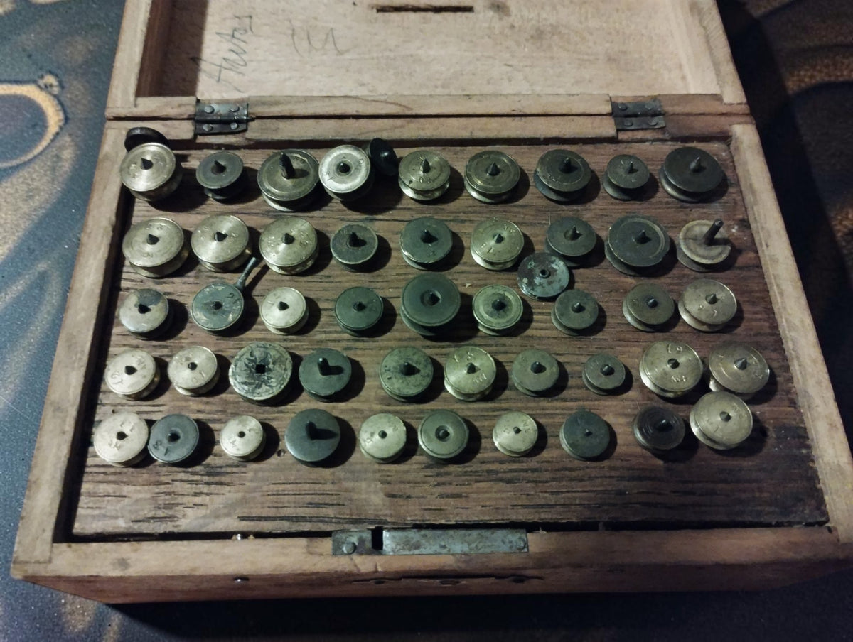 Antique watchmaker’s lantern runner set in an open wooden case, with rows of metal runners in a fitted wooden tray.
