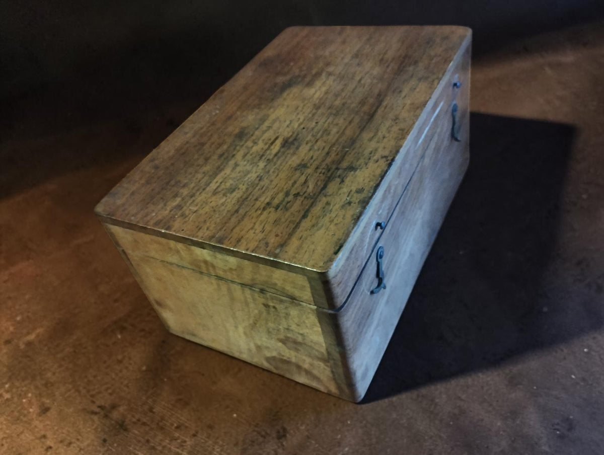 Angled view of the closed wooden cutter case, showing the aged wood, surface wear and metal fastening hooks.
