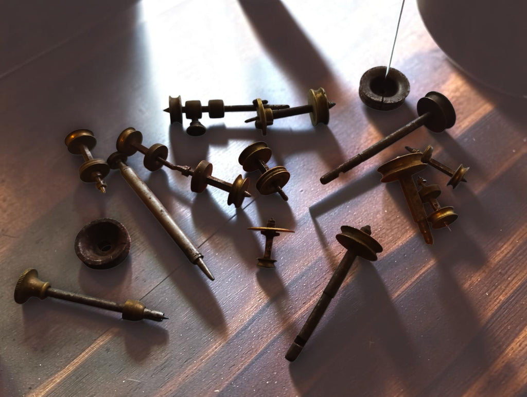 Antique Jacot-tool spare parts arranged on a wooden surface, showing runners, brass pulleys and loose discs
