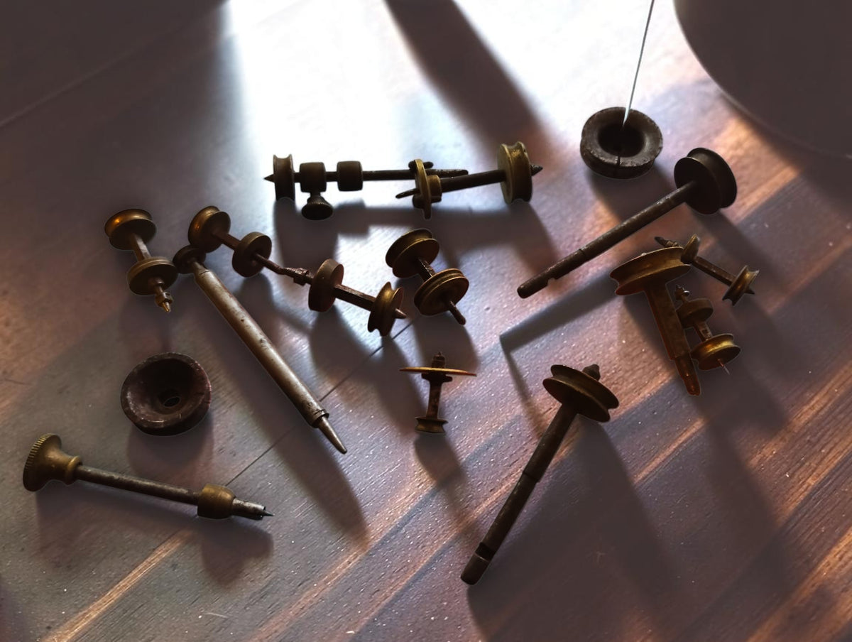 Antique Jacot-tool spare parts arranged on a wooden surface, showing runners, brass pulleys and loose discs
