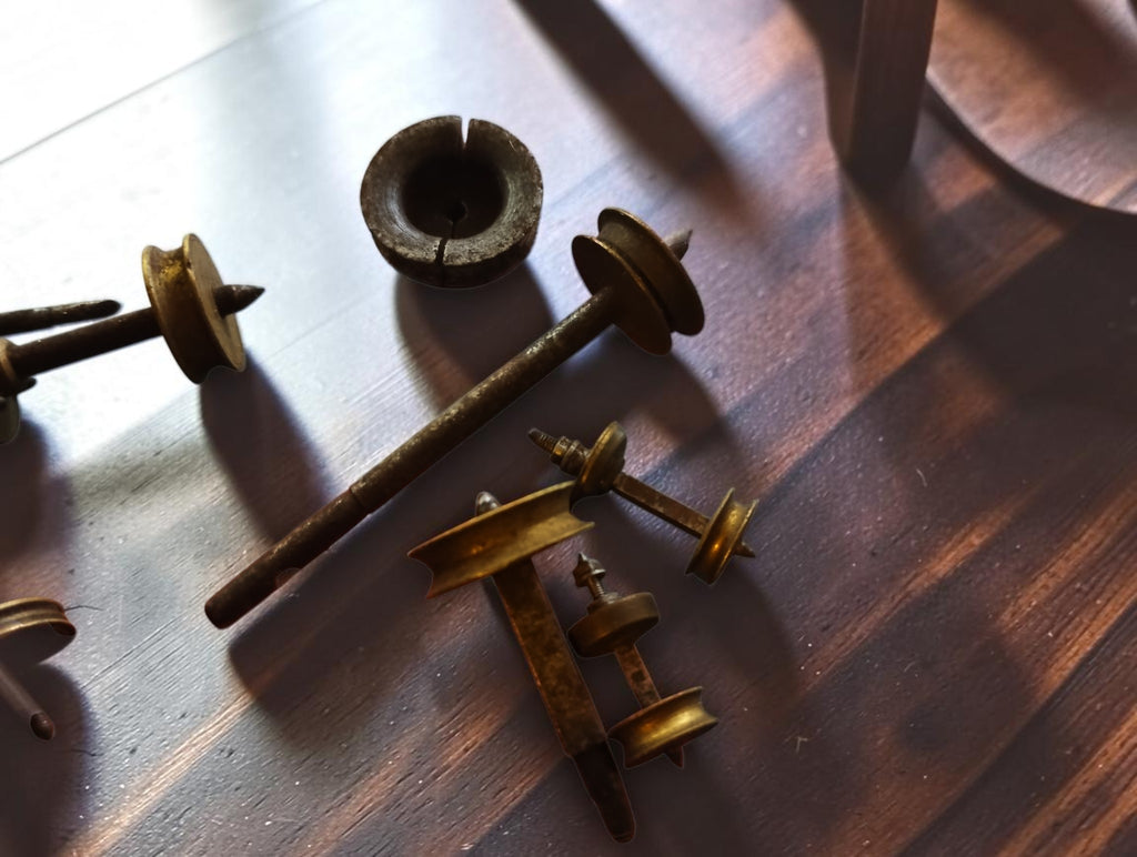 Antique watchmaking tool parts showing a long steel shaft, brass pulleys and a loose circular component
