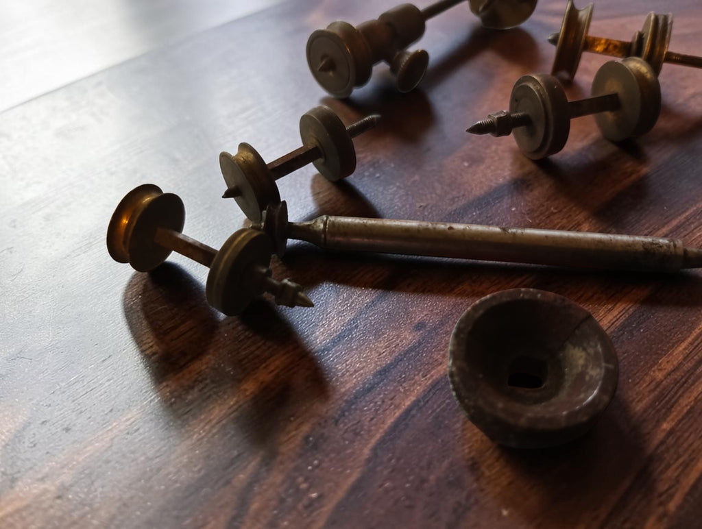 Close-up of antique watchmaking shafts, brass pulleys and a loose disc with visible age and wear

