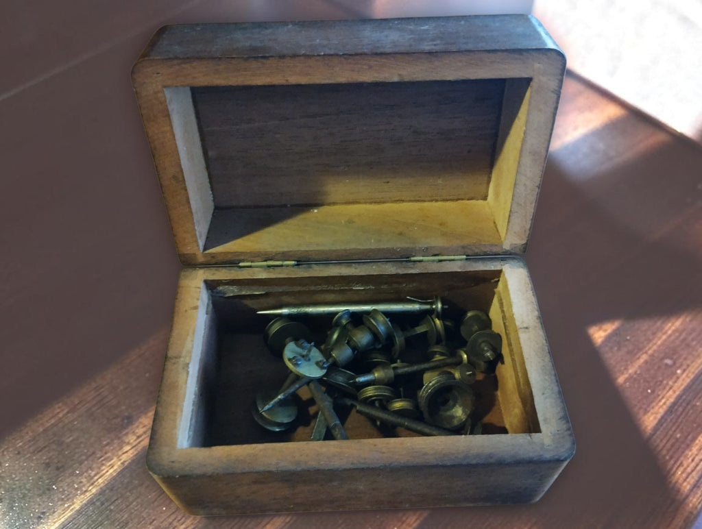 Antique Jacot-tool spare parts with steel runners and brass pulleys inside an open wooden storage box
