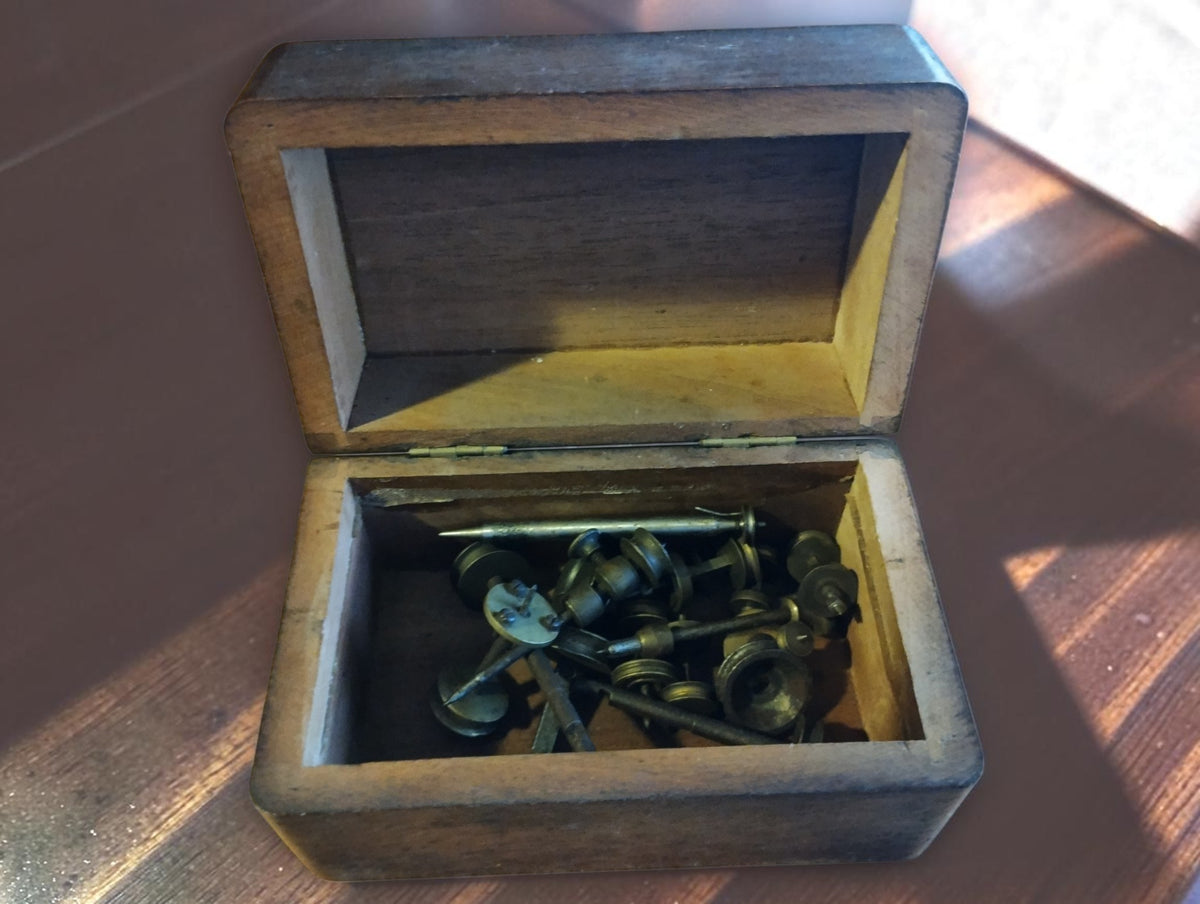 Antique Jacot-tool spare parts with steel runners and brass pulleys inside an open wooden storage box

