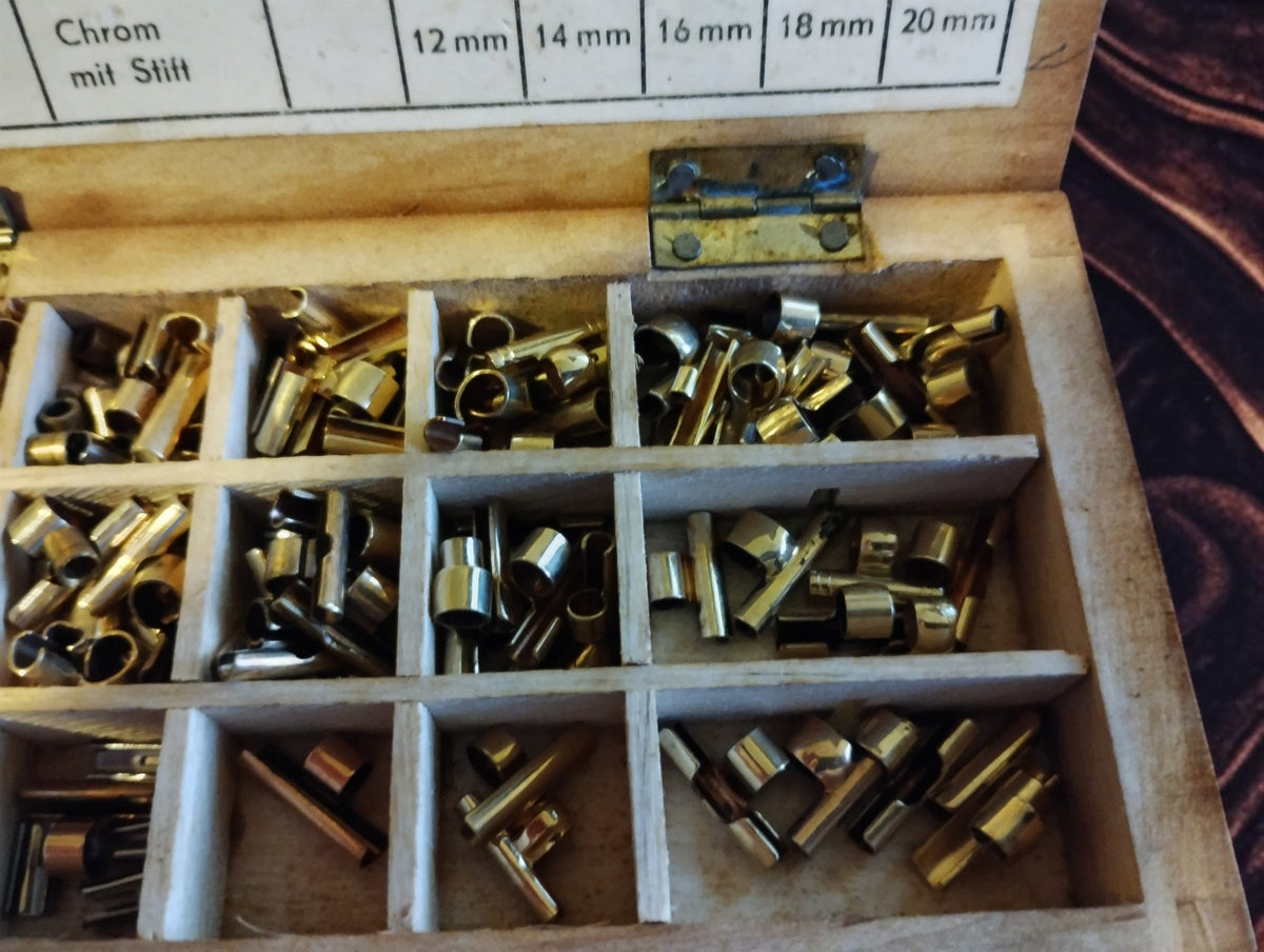 Close-up of assorted metal sleeves and pins in the right compartments of the Ludwig & Fries wooden box.
