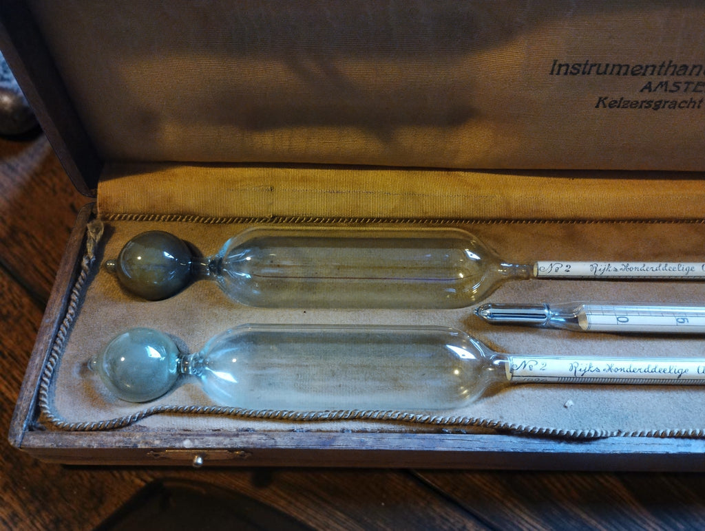 Close-up of two glass alcohol hydrometer bulbs and the thermometer in the fitted, fabric-lined wooden case.
