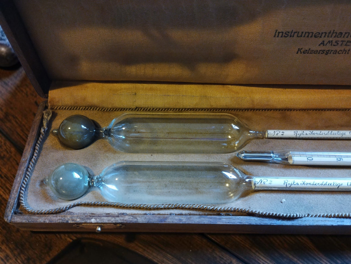 Close-up of two glass alcohol hydrometer bulbs and the thermometer in the fitted, fabric-lined wooden case.
