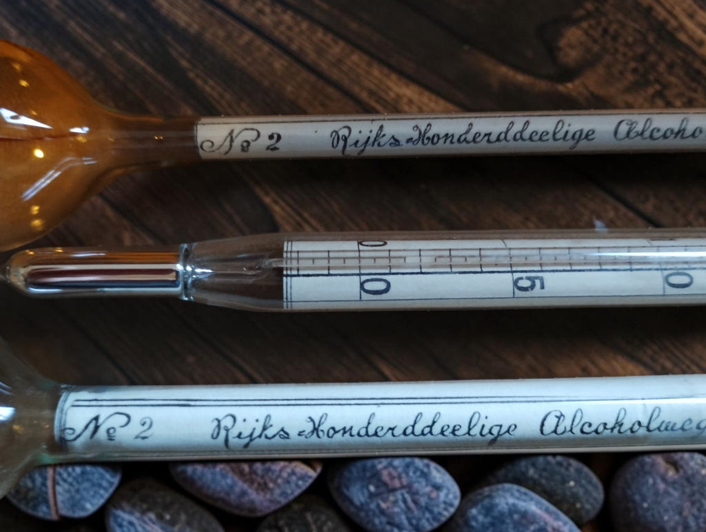 Close-up of the thermometer bulb and scale beside the handwritten labels on the glass alcohol hydrometers.
